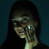 A person in a low-light environment showcasing nail wraps with a glowing design.